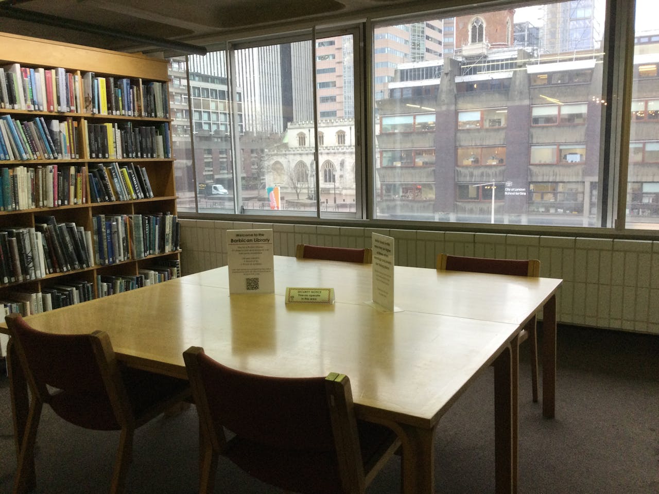 A peaceful library reading room with bookshelves and urban city view through large windows.